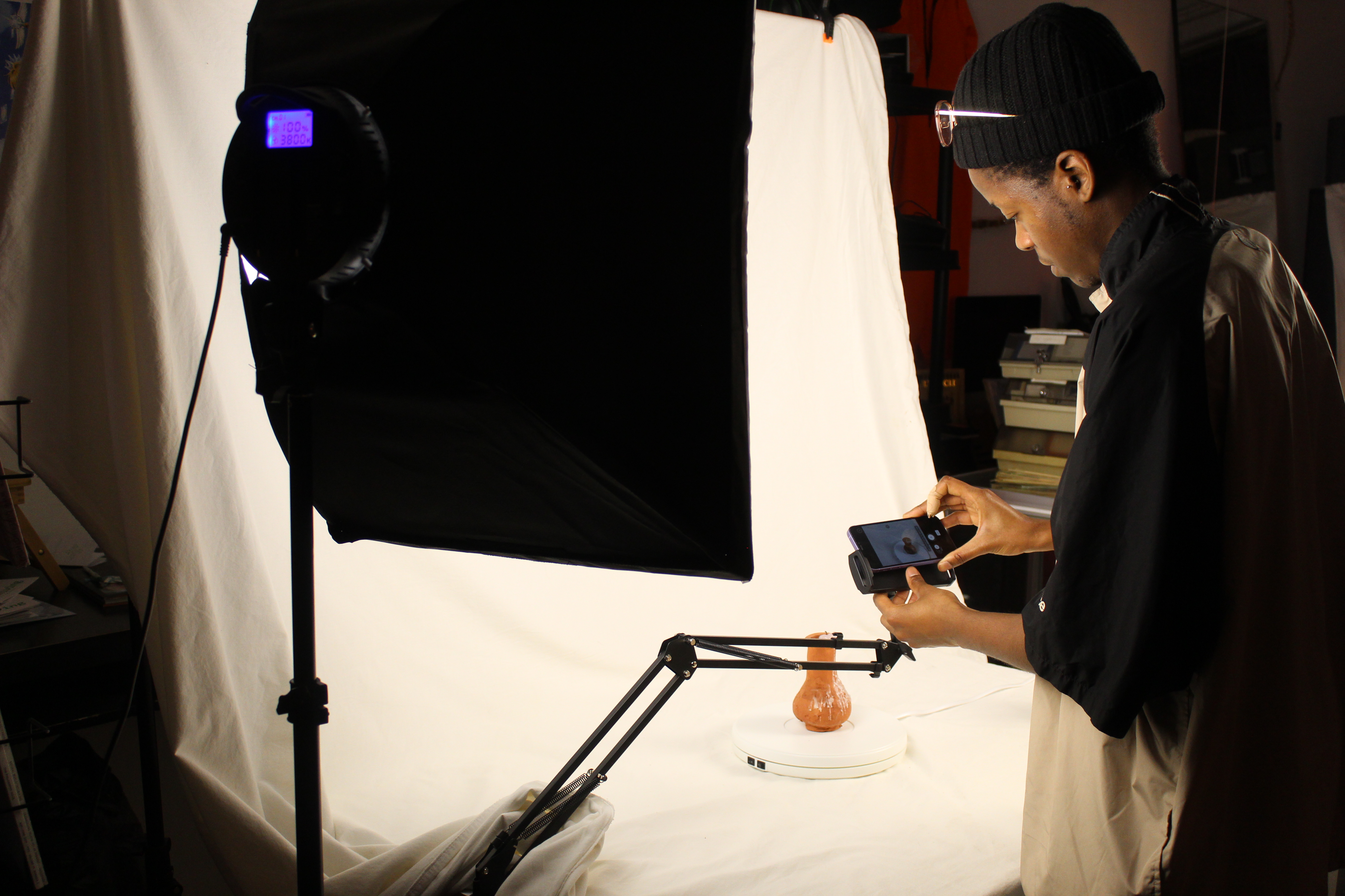 On-site 3D scanning setup with a person photographing a ceramic object on a turntable under studio lights.